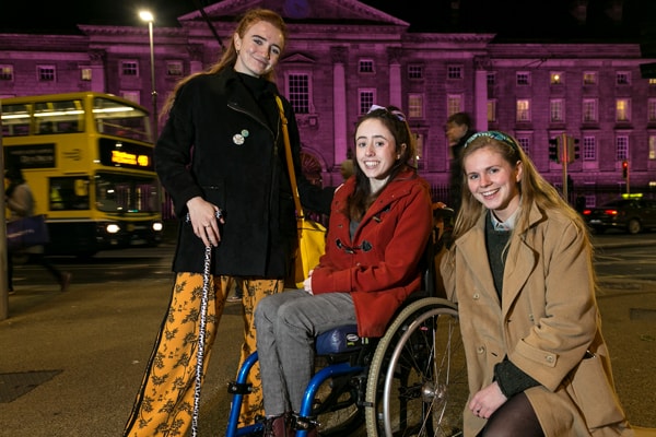 Roísin Hackett, Niamh Ní Hoireabhaird and Laura Beston of Trinity Disability Group, outside a purple TCD