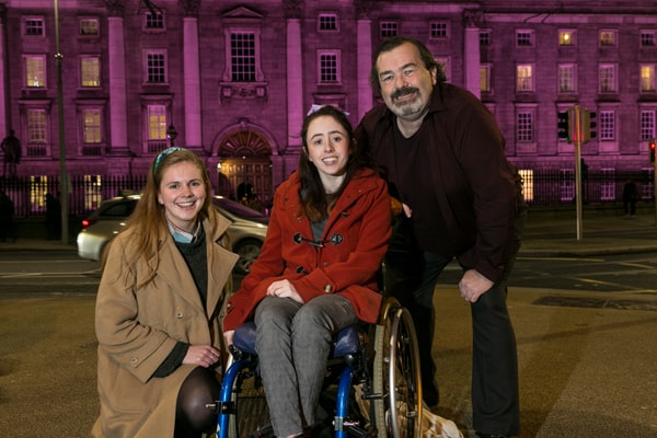 Laura Beston, Niamh Ní Hoireabhaird and disability activist Gary Kearney outside a purple TCD