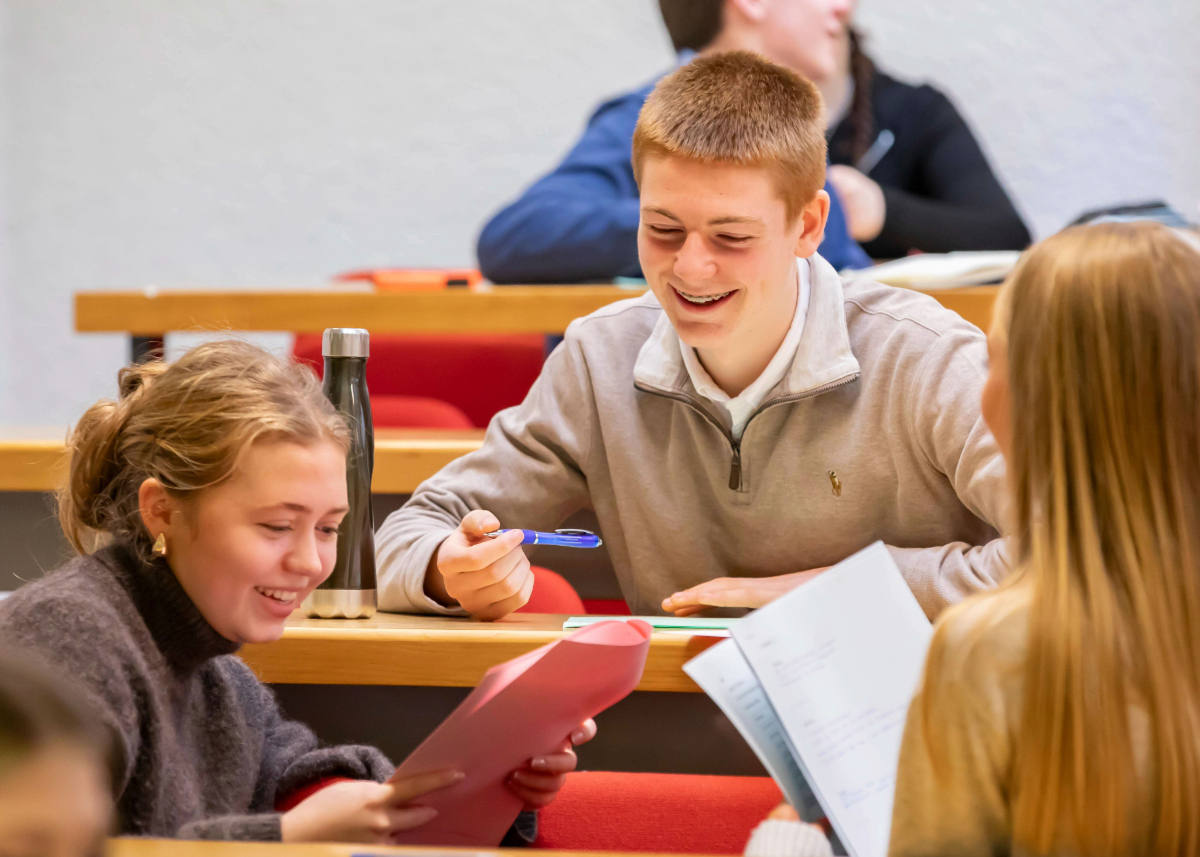Students seated in a lecture hall working together on an activity, holding papers and discussing their work.