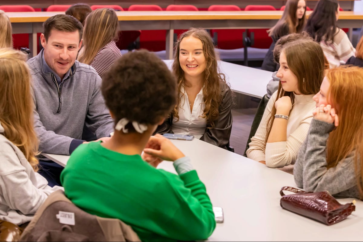 A small group of students and a facilitator gathered around a table in a classroom setting, taking part in a discussion during a collaborative learning activity.