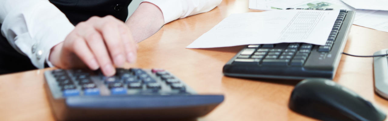 A female hand using a calculator with a keyboard nearby