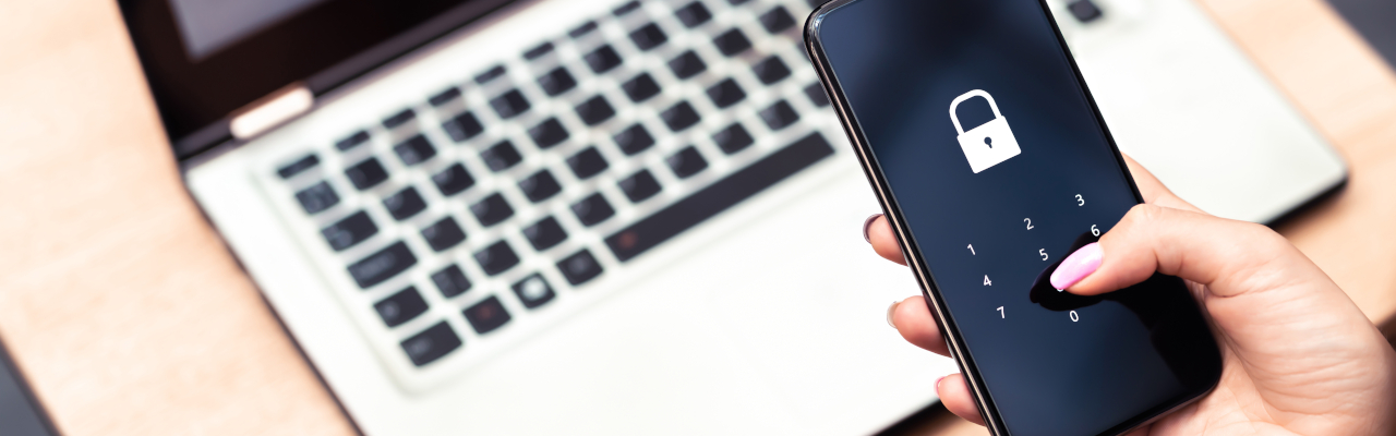Cyber security: a female hand holds a smartphone entering a secure PIN code over a laptop
