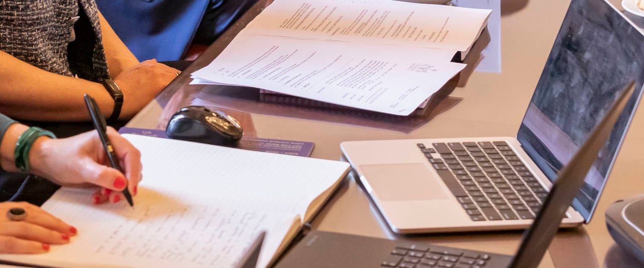 A decorative image: Female hand taking notes while looking at a computer screen