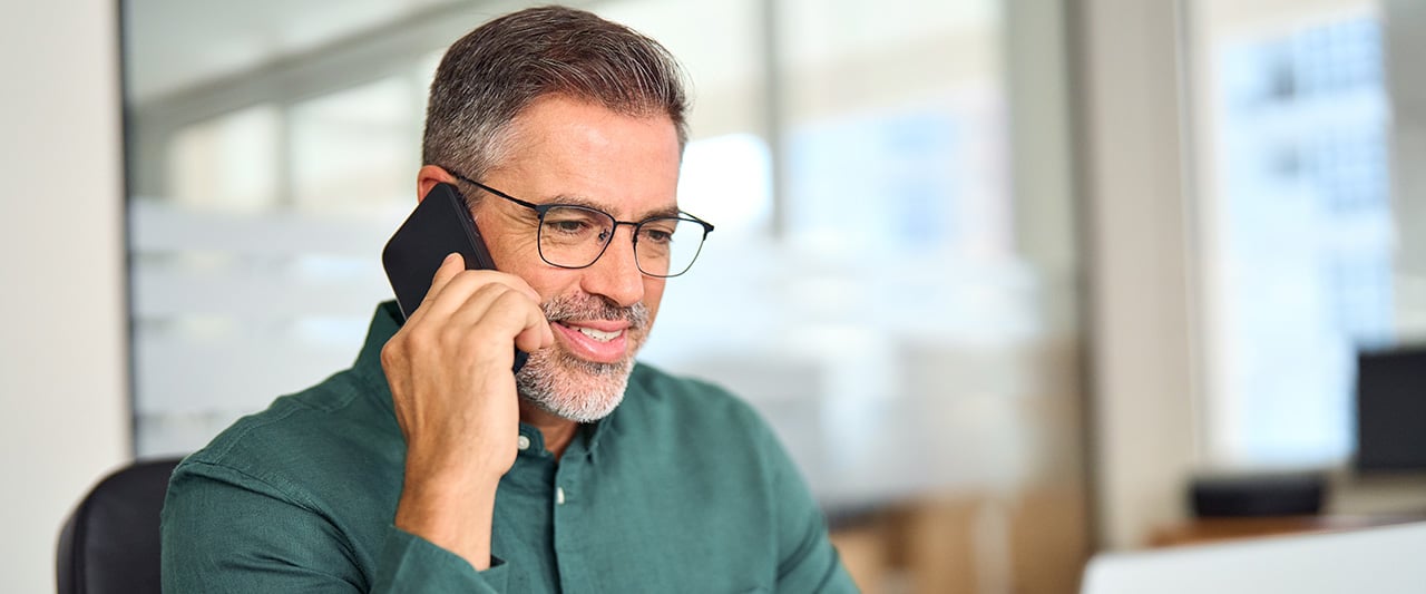 A male pforessional talking on the phone, having a pleasant conversation