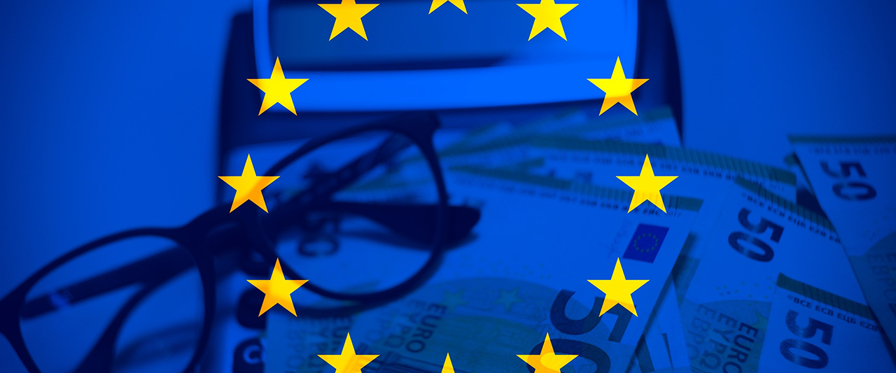 Glasses next to an EU flag with money under scrutiny