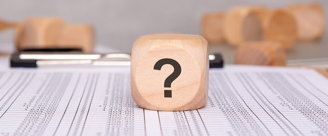 A wooden cube with a question mark on a spreadsheet